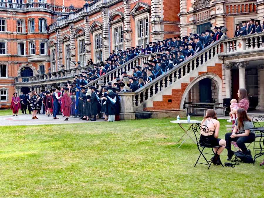 A large group of graduates outside a historic university building during a graduation ceremony in England.
