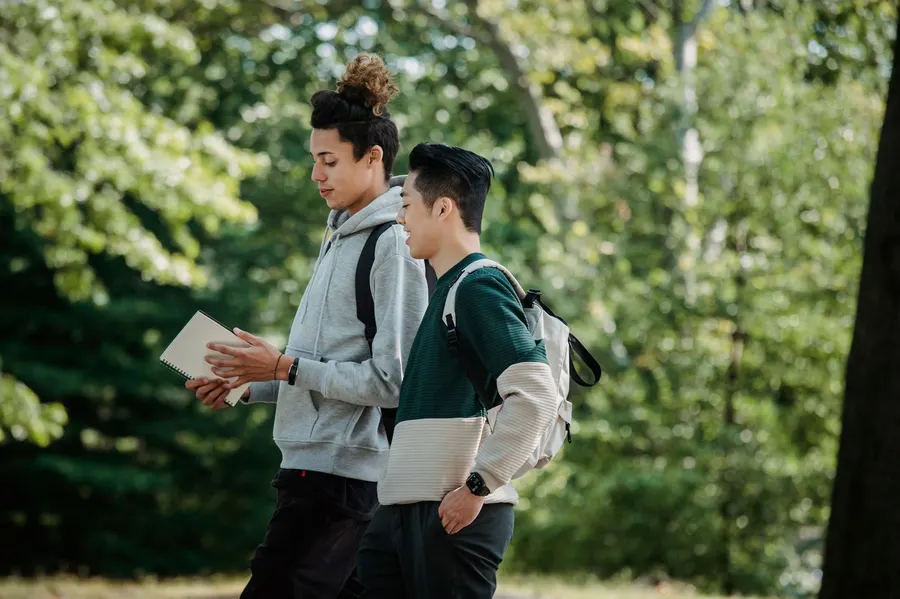 Side view of positive multiethnic classmates with backpacks and notepad walking in university park