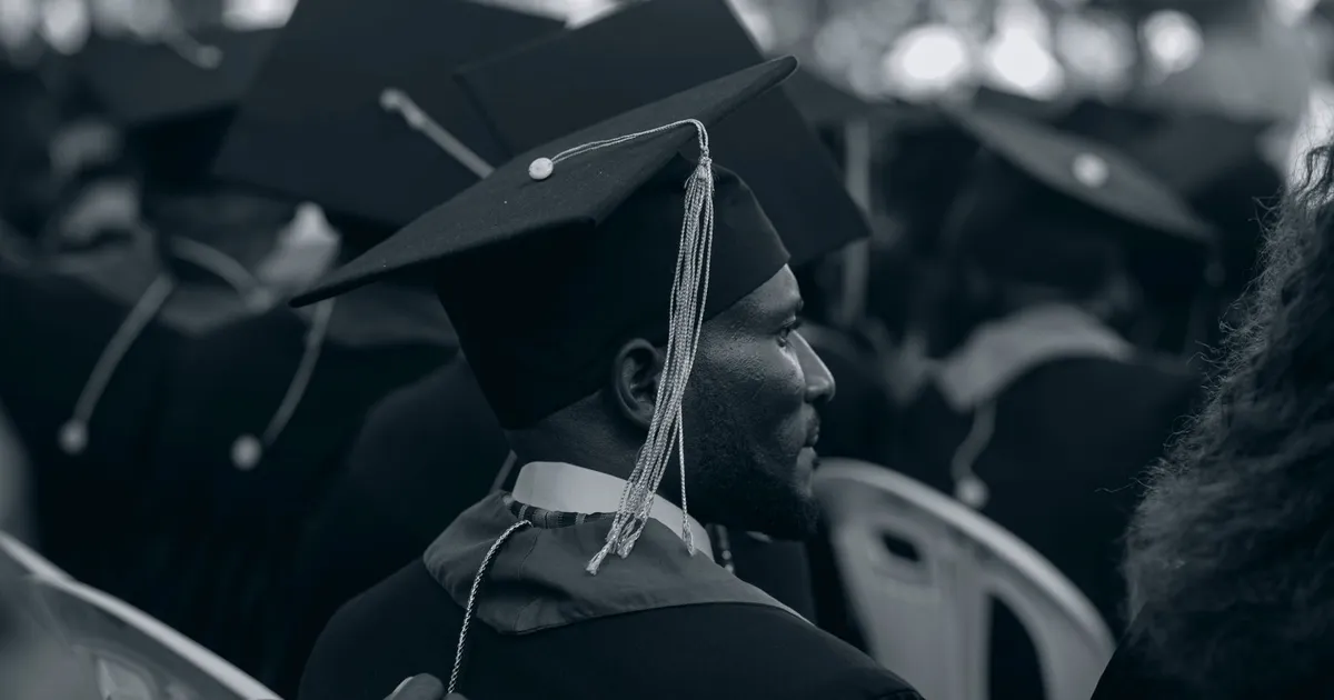 Black and white photo of graduates in caps and gowns at a ceremony.