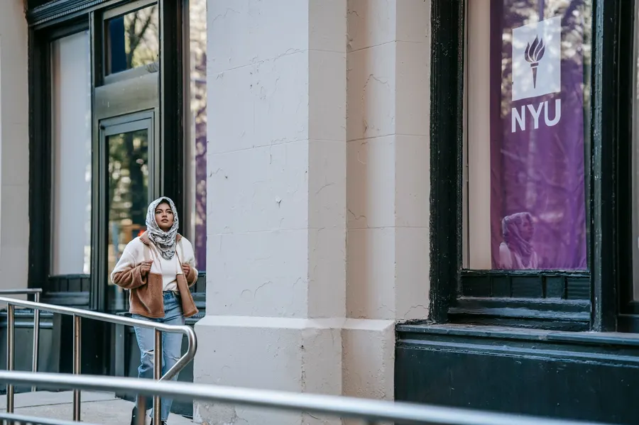 Focused young ethnic female traveler in stylish outfit and hijab sightseeing city while walking near modern building during holidays