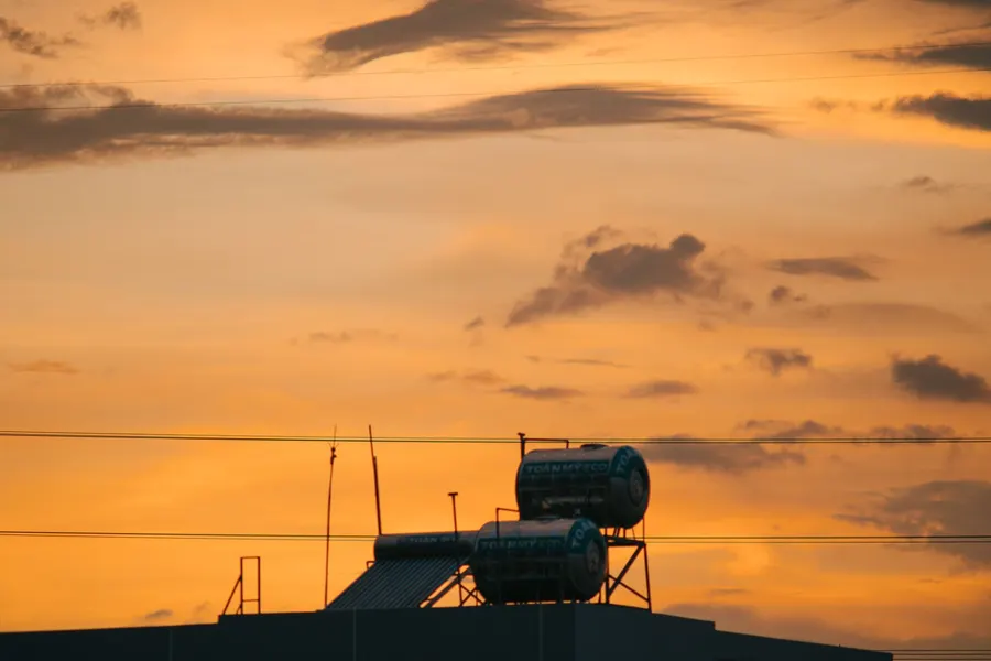 Sunset silhouette of an industrial rooftop against orange sky with tanks and antennas.