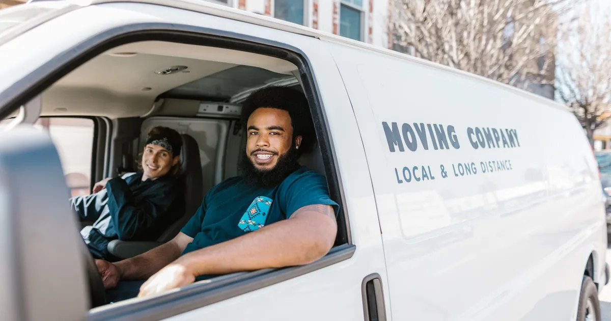 Two movers smiling from their moving company van parked on a sunny day.