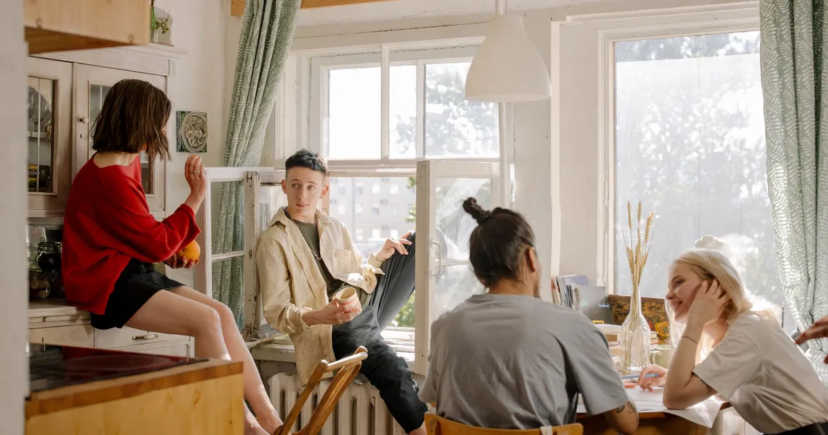 Group of young friends relaxing and chatting in a sunlit kitchen space.