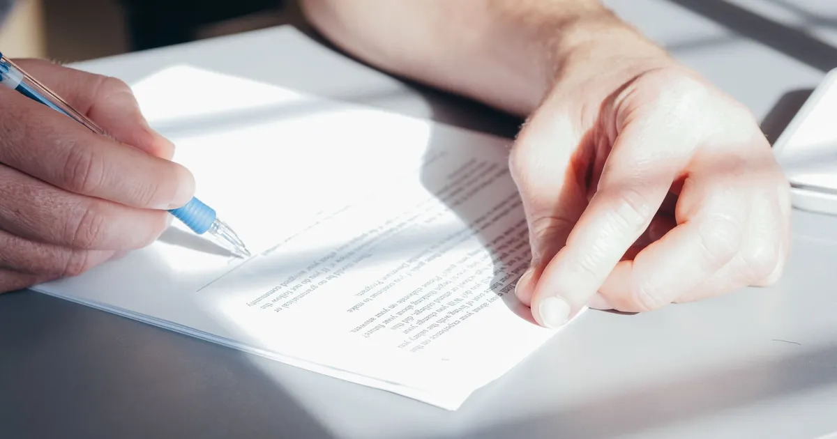 Hands signing a contract with a blue pen, close-up view.