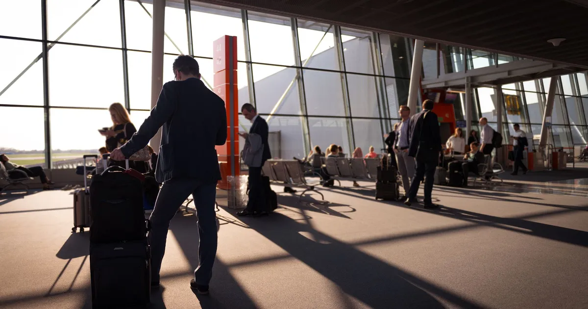 Travelers in a bustling airport terminal with carry-on luggage waiting for departure.