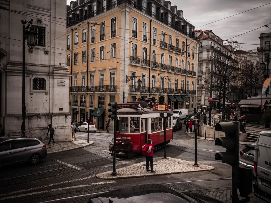 A historic red tram navigates a charming street in Lisbon's bustling downtown, showcasing classic architecture.