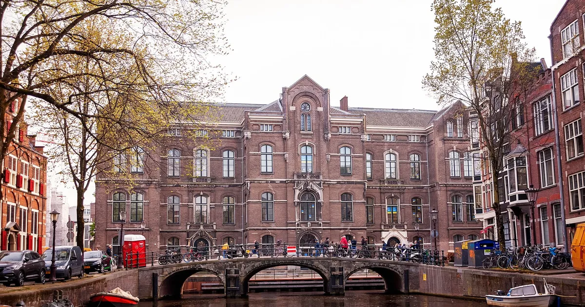 Historic Amsterdam canal with bridge and building facade, vibrant spring atmosphere.