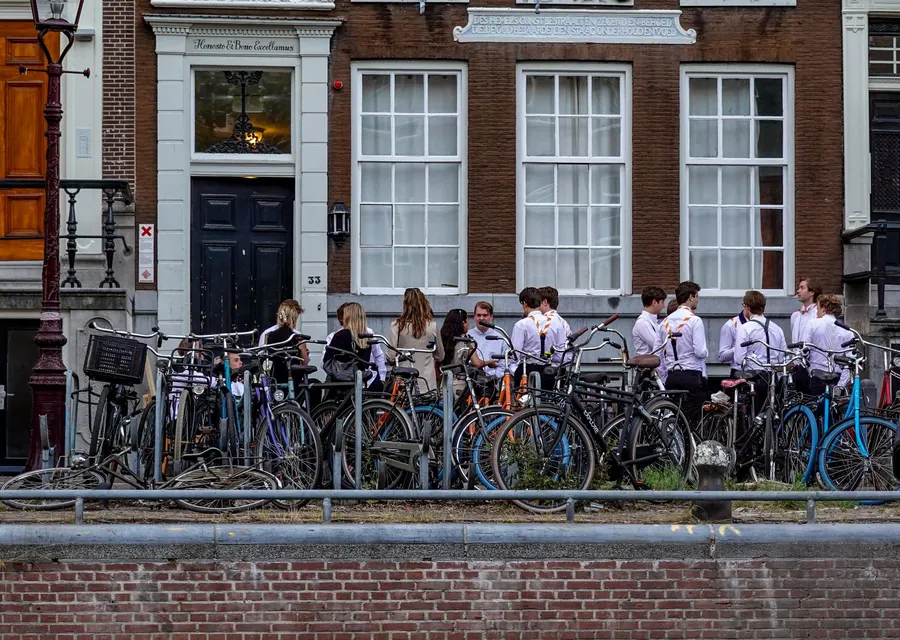 A group of young adults in Amsterdam, Netherlands, with bicycles against a historical building on a city street.
