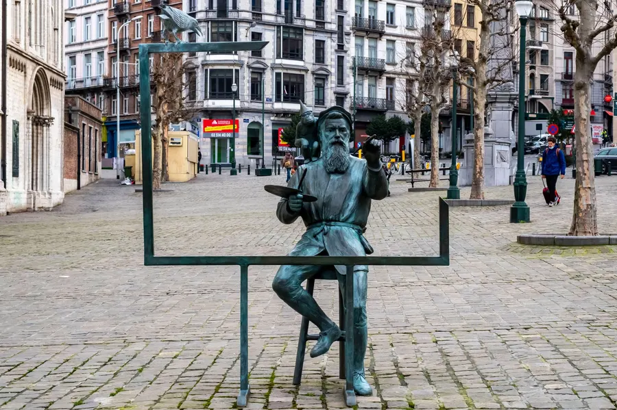 Bronze sculpture of an artist painting, set on a cobblestone street in a European city square.
