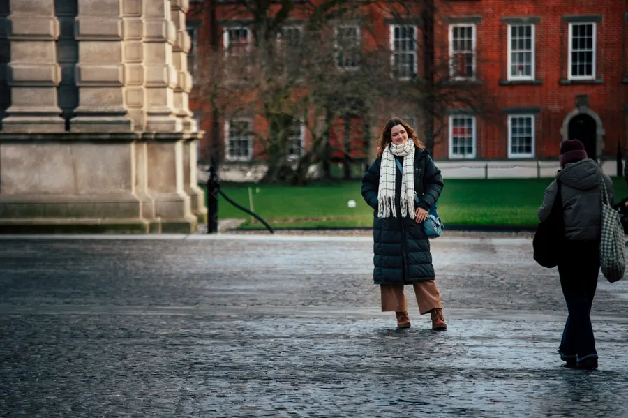 Woman in winter attire poses in Dublin's historic university square.