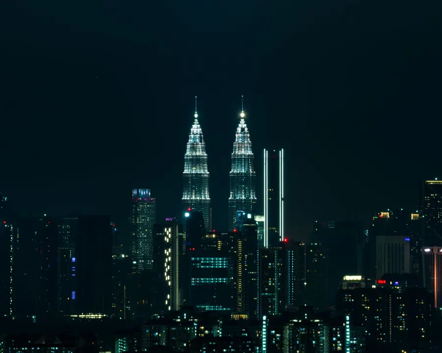 Breathtaking view of Kuala Lumpur's skyline at night featuring the iconic Petronas Towers illuminated against a dark sky.