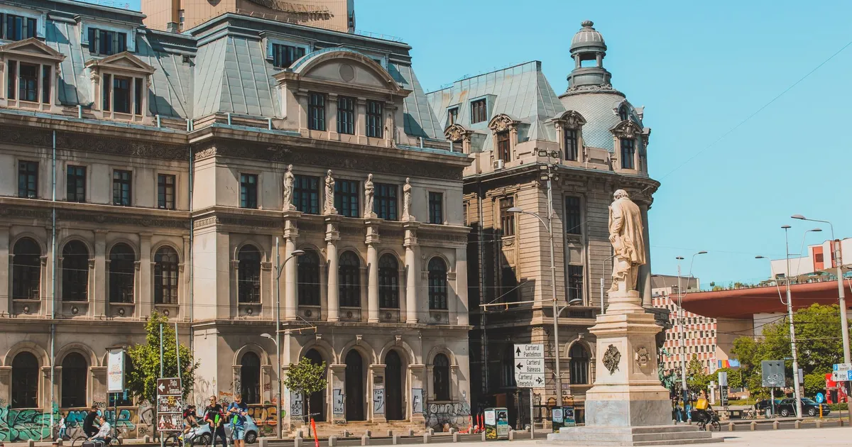 Elegant historic buildings with a statue under a clear blue sky in Bucharest, Romania.