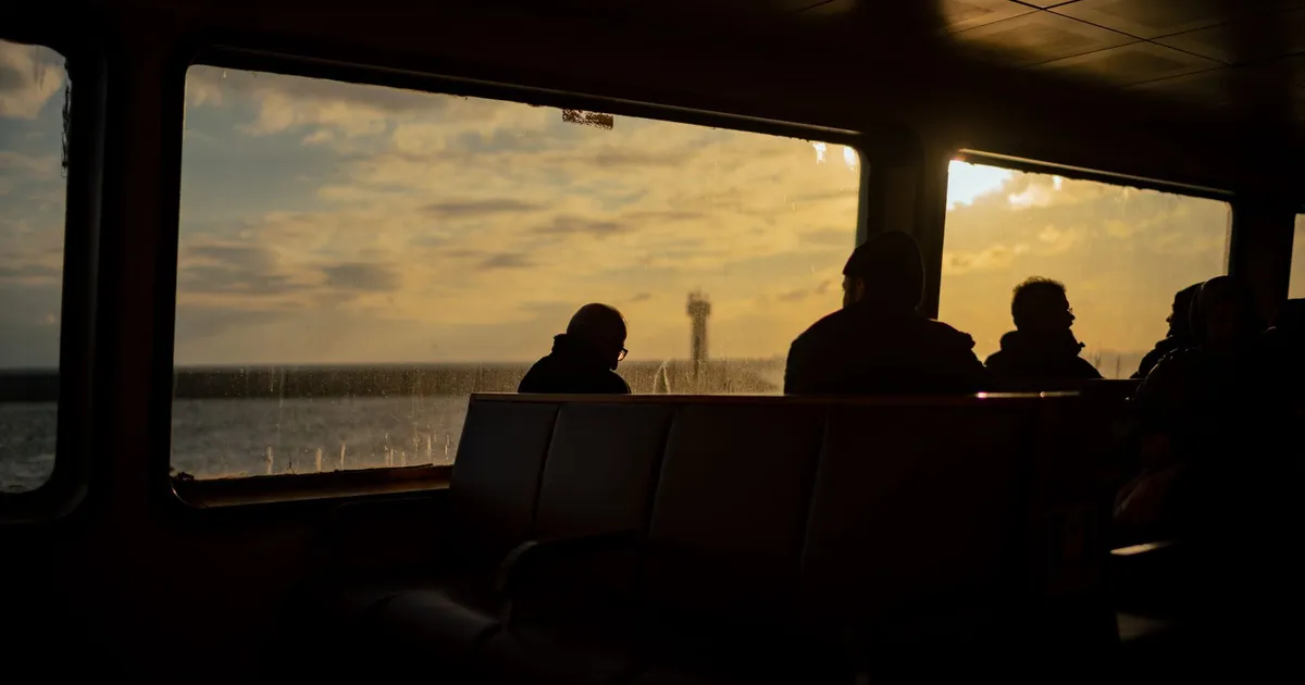 Silhouettes of passengers inside a ferry during sunset, viewing the sea outside.