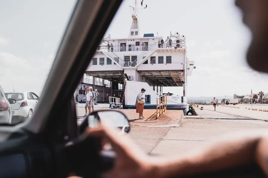 Passengers board a ferry at a Sardinia harbor, captured from a car's perspective.