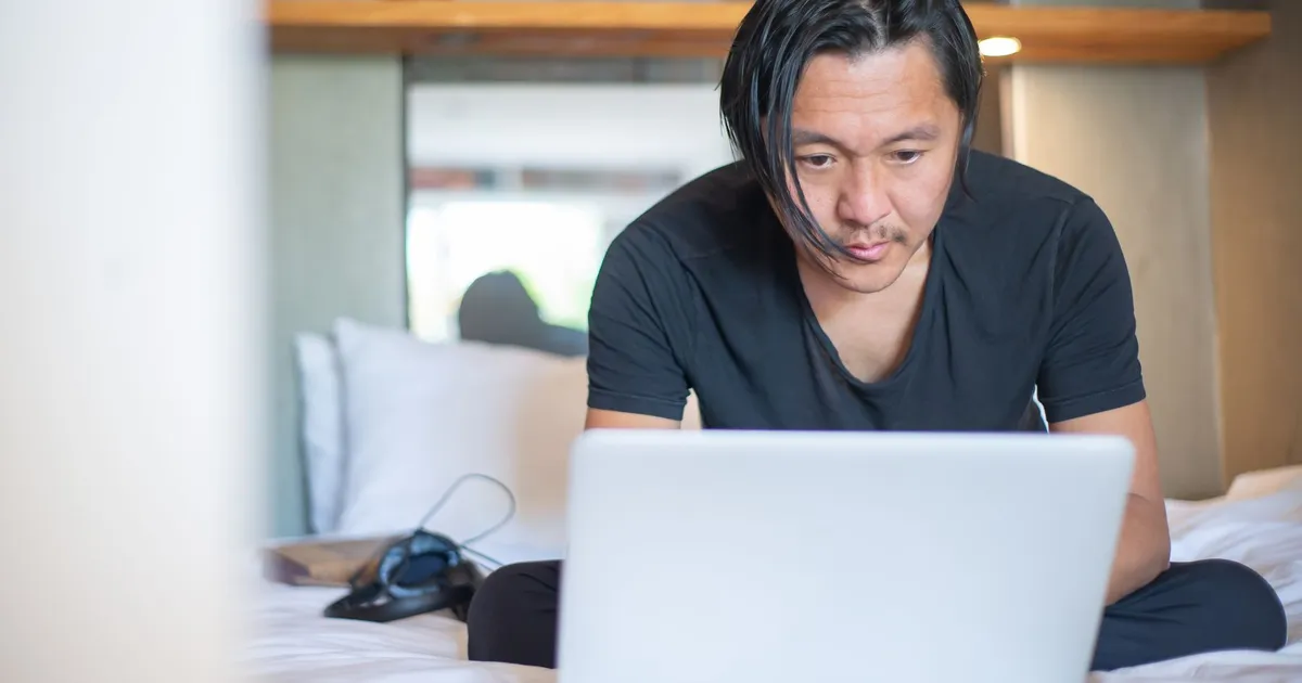 An Asian man working from home on a laptop, focusing on his digital tasks in a cozy indoor setting.