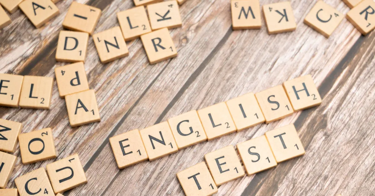 Wooden Scrabble tiles spelling out 'English Test' on a wooden background, ideal for language exam themes.