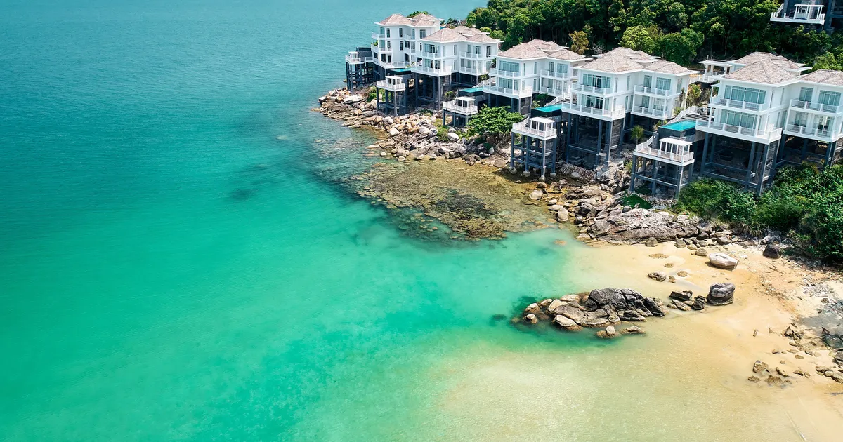 Luxury villas perched on a rocky coast with turquoise sea, offering a tropical paradise feel.