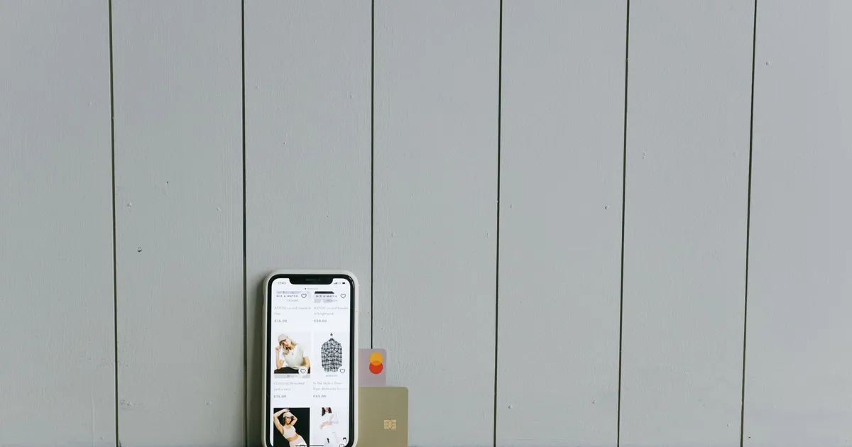 A smartphone displaying an ecommerce site with a credit card, set on a wooden surface, depicting online shopping.