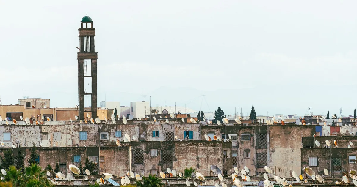 Urban rooftops with satellite dishes beneath a towering minaret in Tunis, Tunisia.