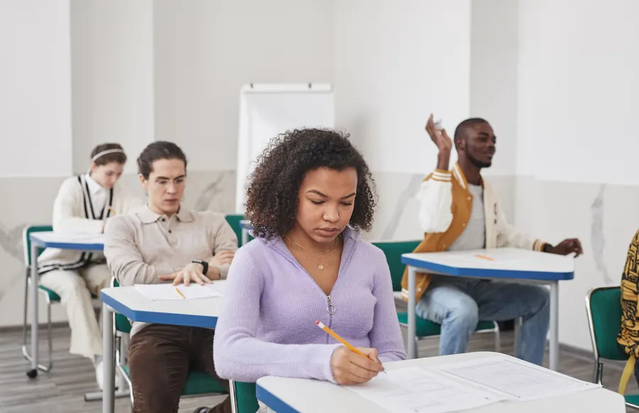 Group of diverse students focusing on exam in classroom setting.