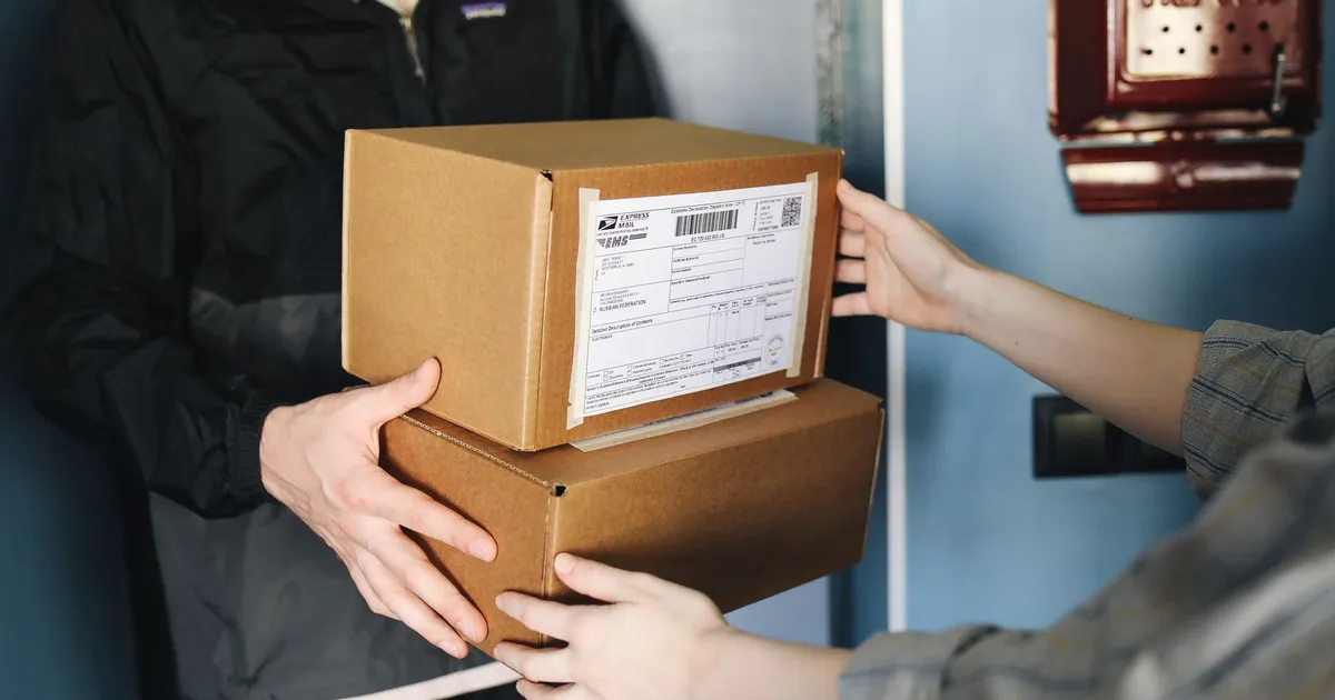 Close-up of hands exchanging cardboard boxes indoors, symbolizing delivery service.